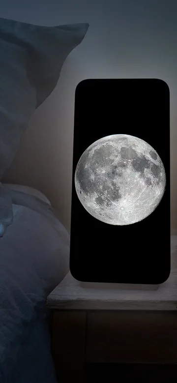 Visuel officiel de Night Light montrant une pleine lune sur l’écran d’un iPhone posé près d’un lit.